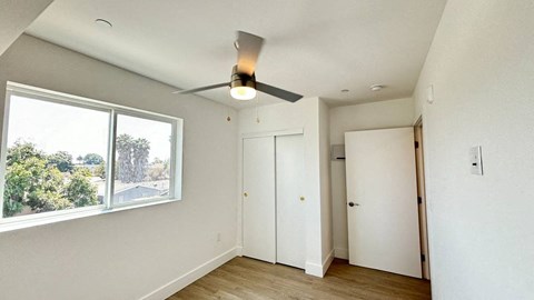 A room with a ceiling fan and a window overlooking a tree-filled street.