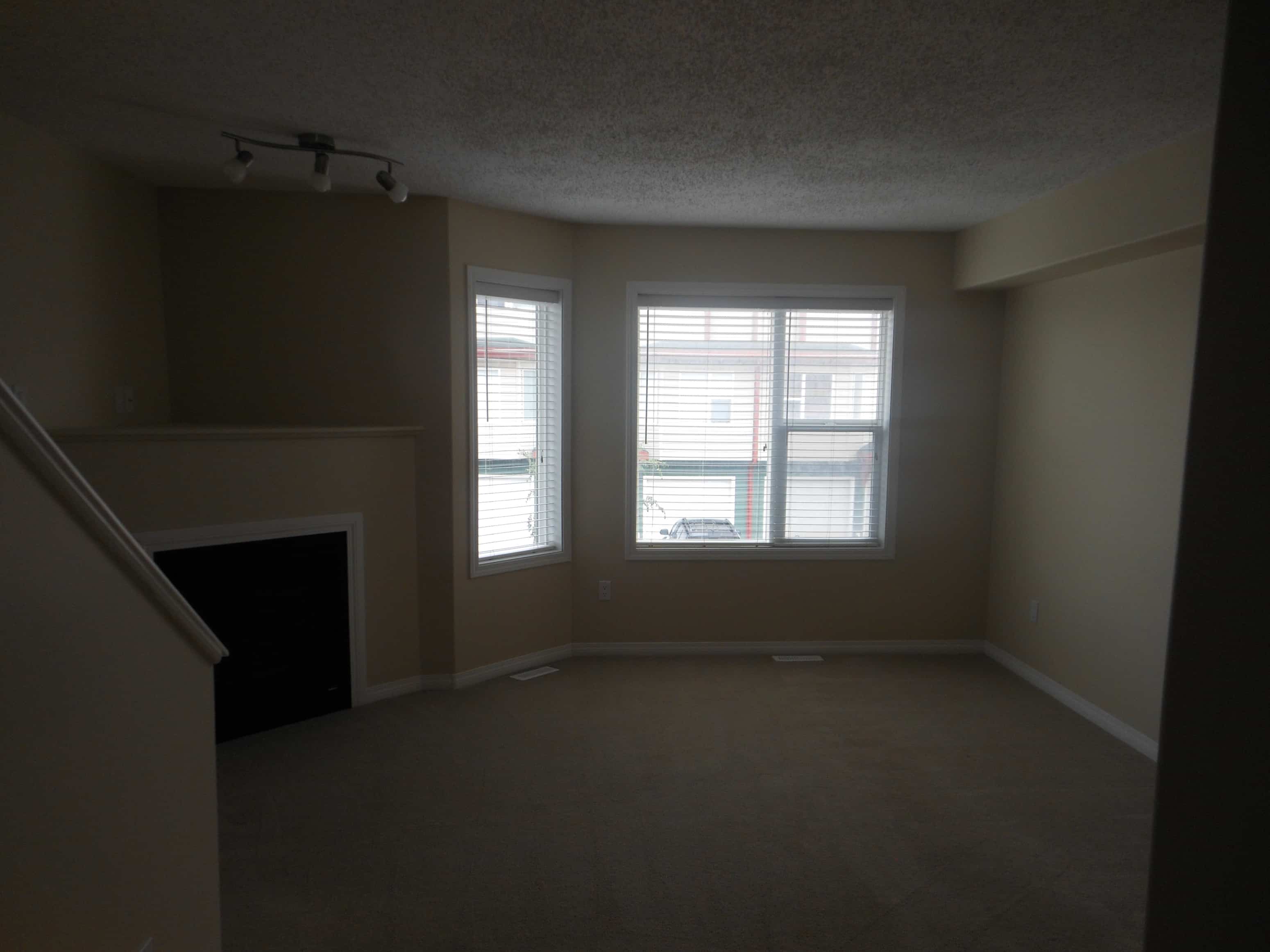 an empty living room with two windows and a fireplace