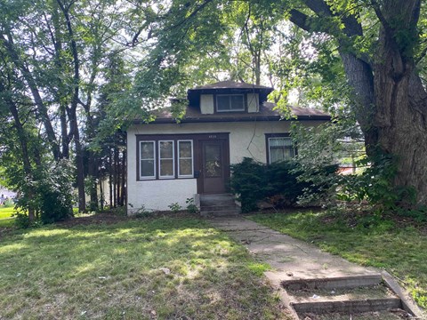 a small white house with trees and a sidewalk