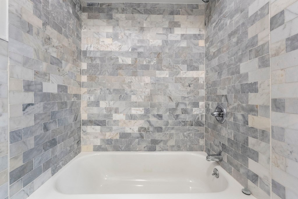 a bathroom with a tub and a tiled wall and a shower