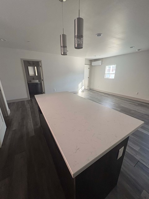 A kitchen with a white counter top and dark wood flooring.