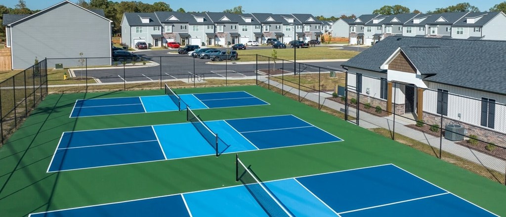 A tennis court with blue and green surface and white buildings in the background.