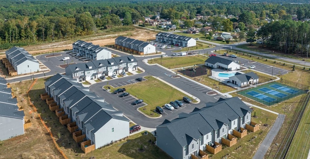 A large aerial view of a housing complex with multiple houses and a swimming pool.