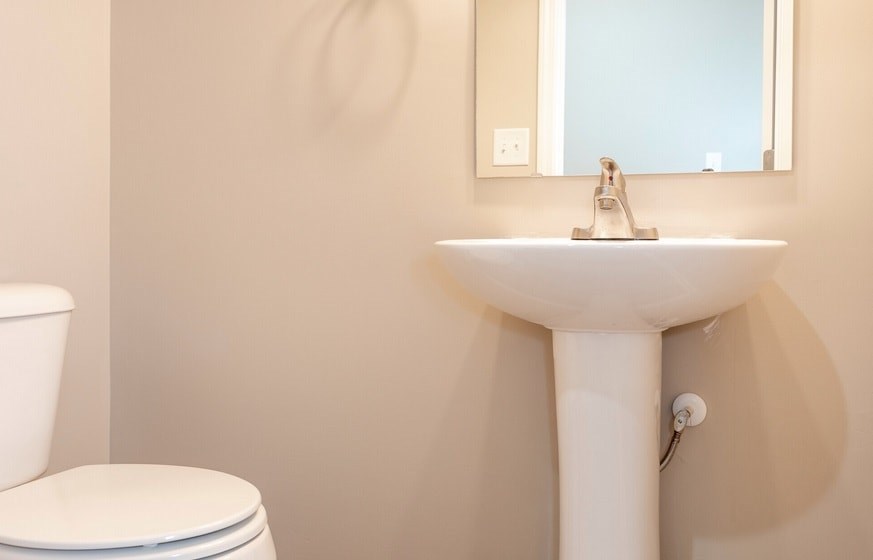 A white sink in a bathroom with a toilet and mirror.