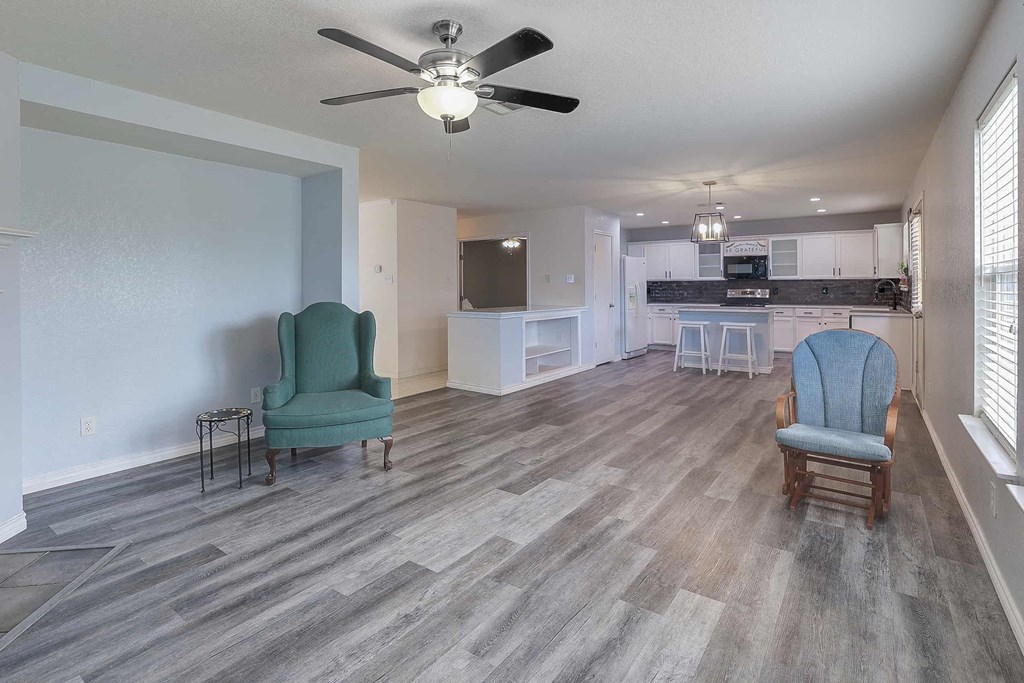 a living room and kitchen with chairs and a ceiling fan