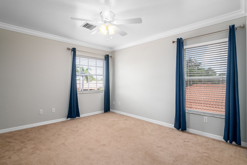 an empty living room with two windows and a ceiling fan