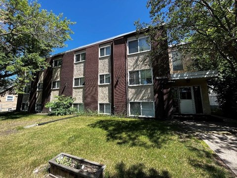 a brick apartment building with a green yard in front of it