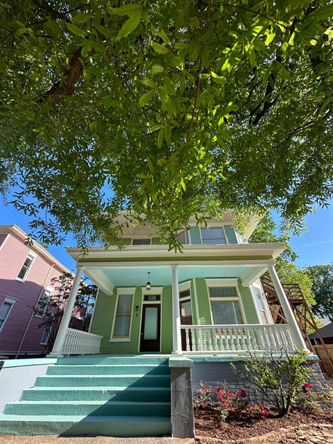 a green house with stairs and a tree in front of it