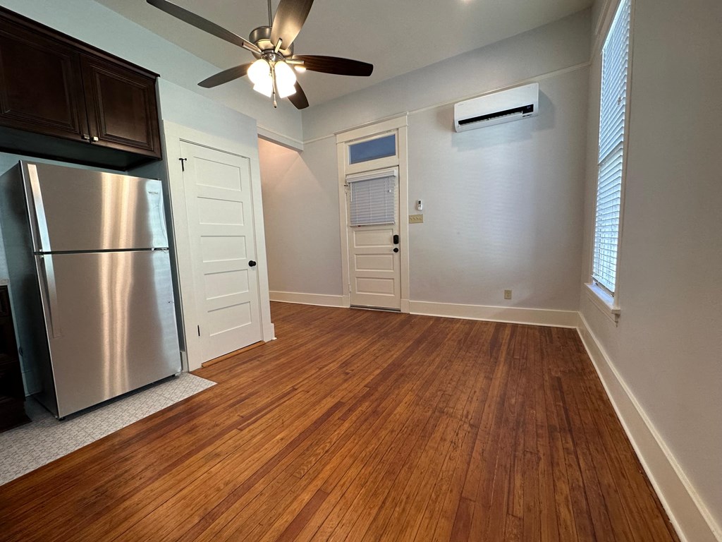 an empty living room with a refrigerator and a ceiling fan