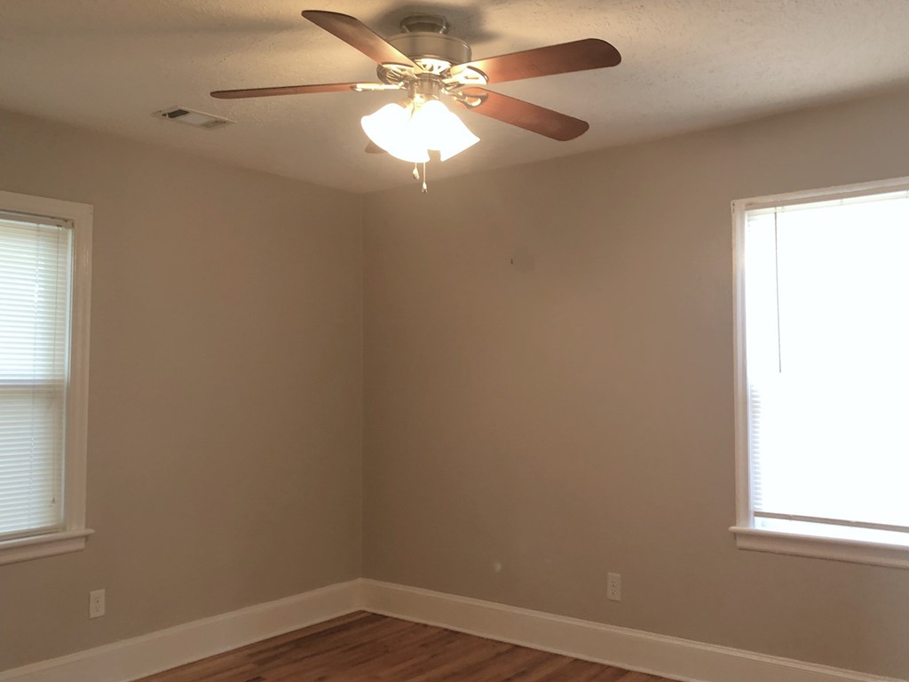 a bedroom with a ceiling fan and two windows