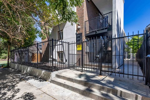 A black metal fence surrounds a building with a brick wall and a balcony.