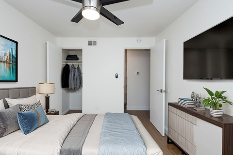 A bedroom with a bed, a ceiling fan, and a cabinet with a plant on it.