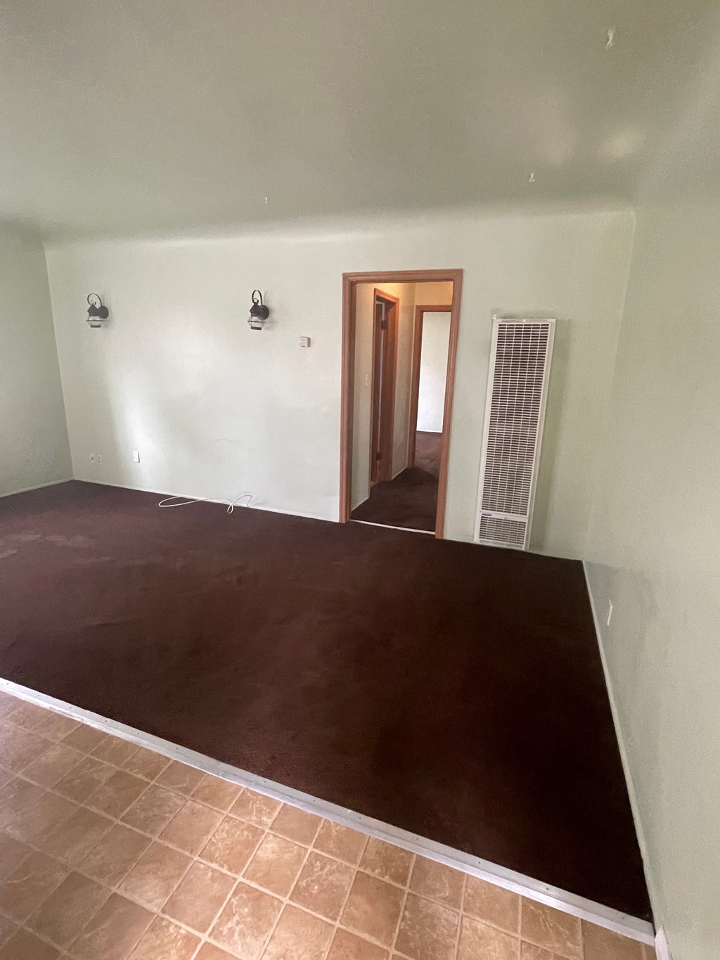 an empty living room with a brown tile floor and white walls