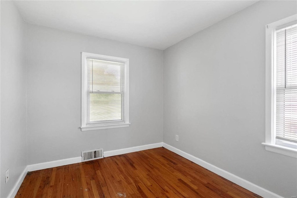 an empty room with wooden floors and two windows
