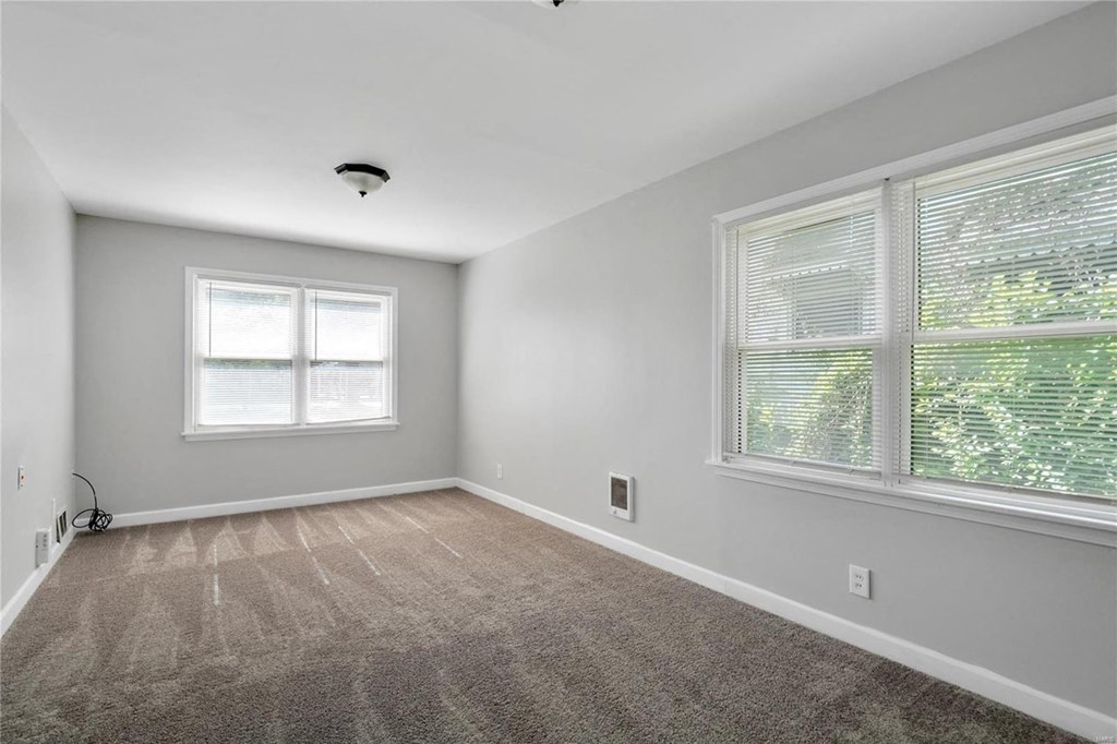 an empty living room with two windows and a carpet