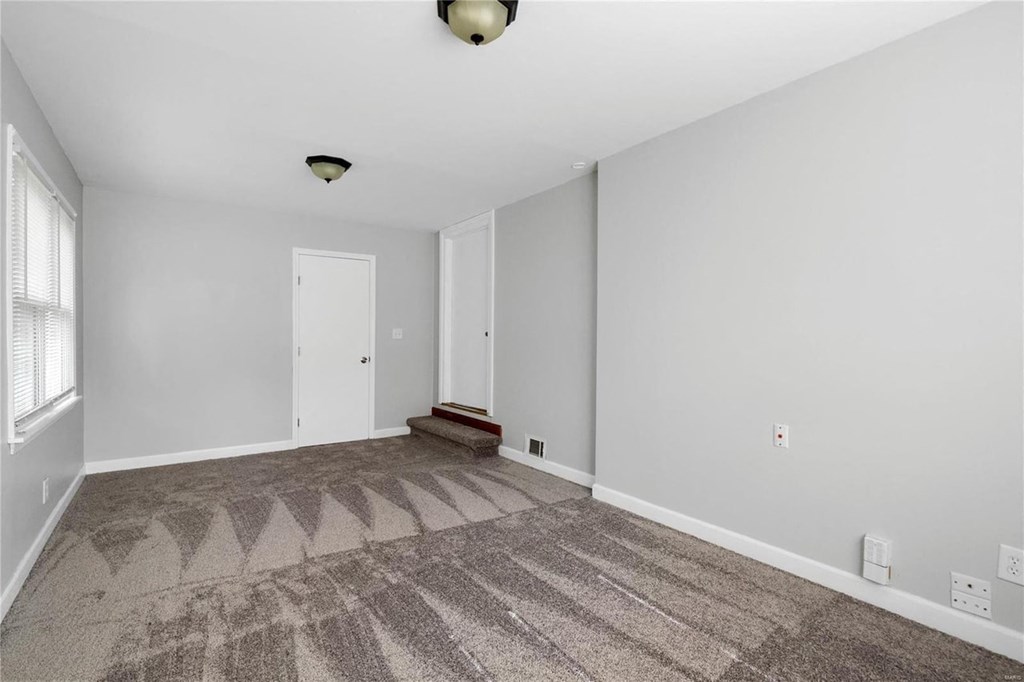 a empty living room with carpet and a door to a bedroom
