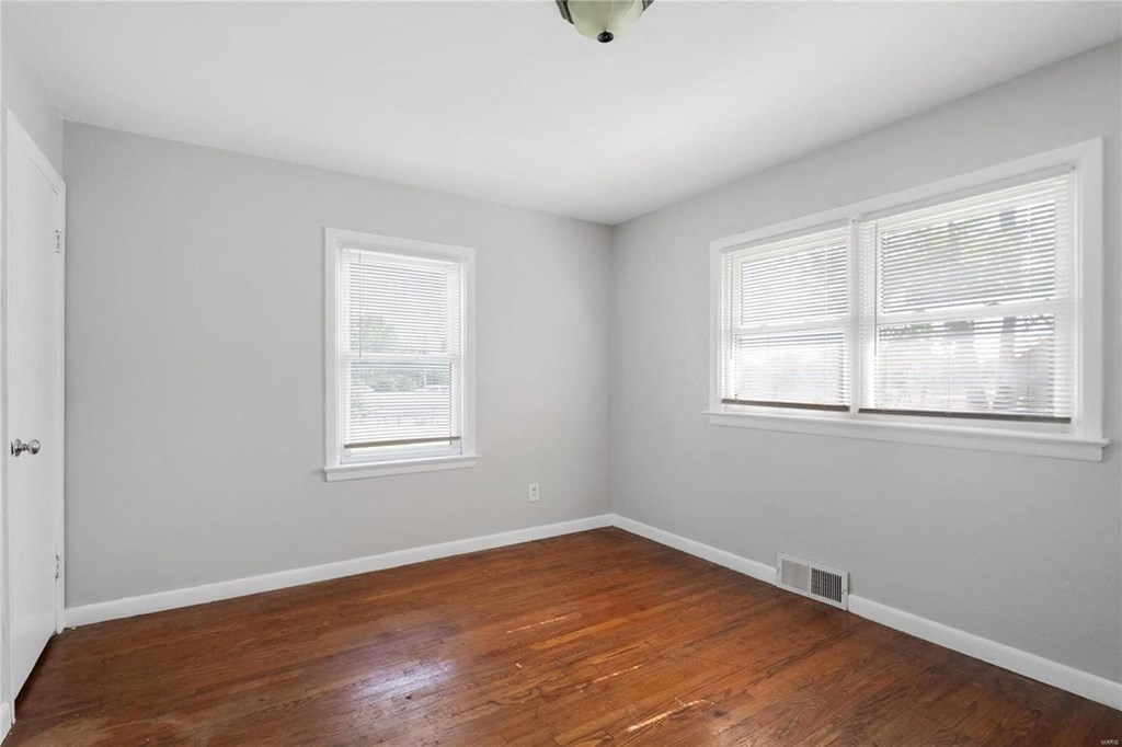 an empty room with wood floors and two windows