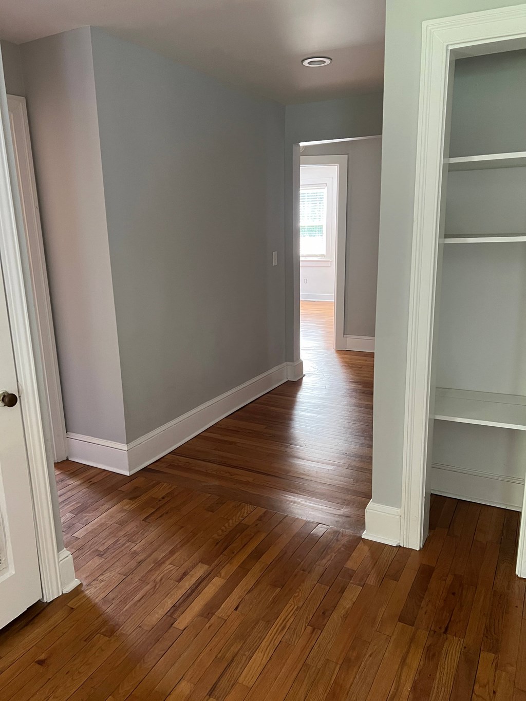 a hallway with a hard wood floor and grey walls and white shelves