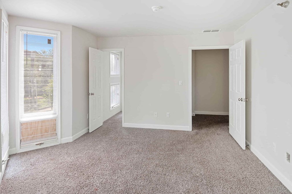 A room with white walls and carpeted floor with a window on the left side.