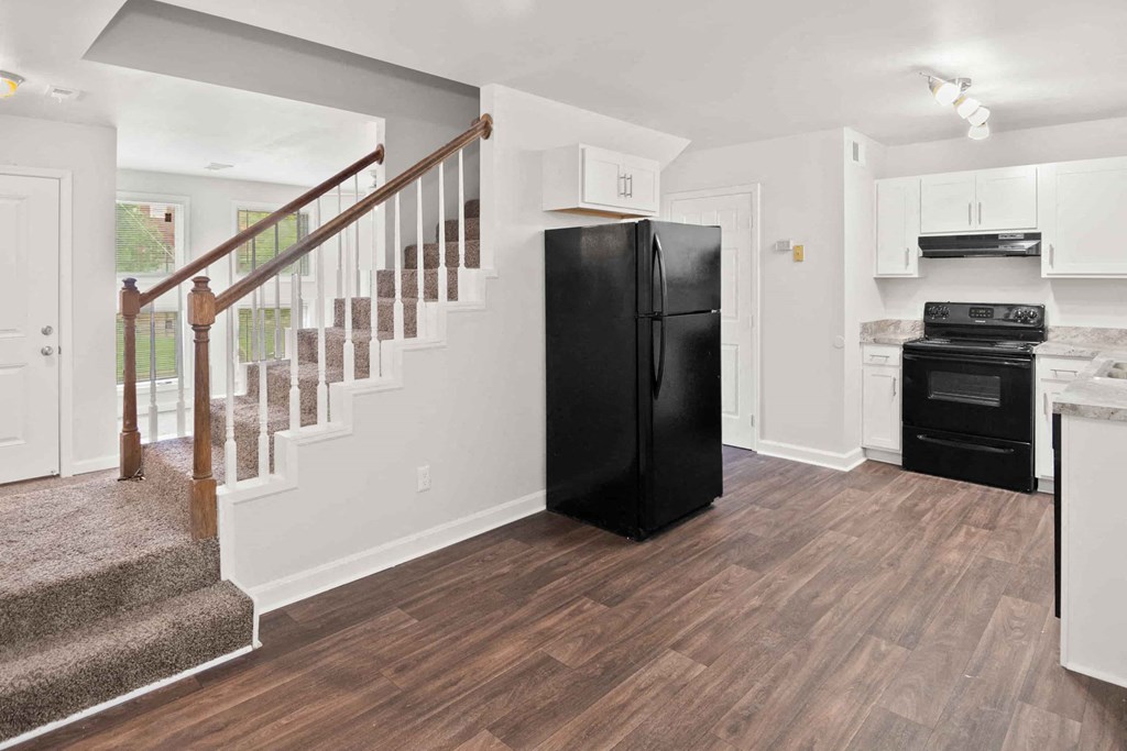A black refrigerator in a kitchen with wooden floors and white walls.