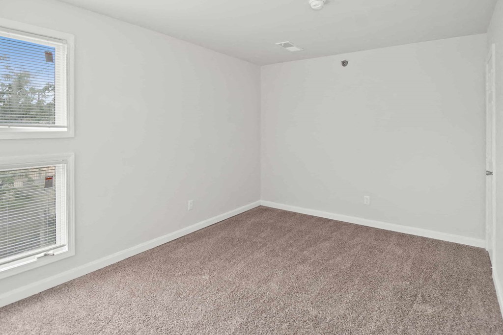 A room with a carpeted floor and two windows.