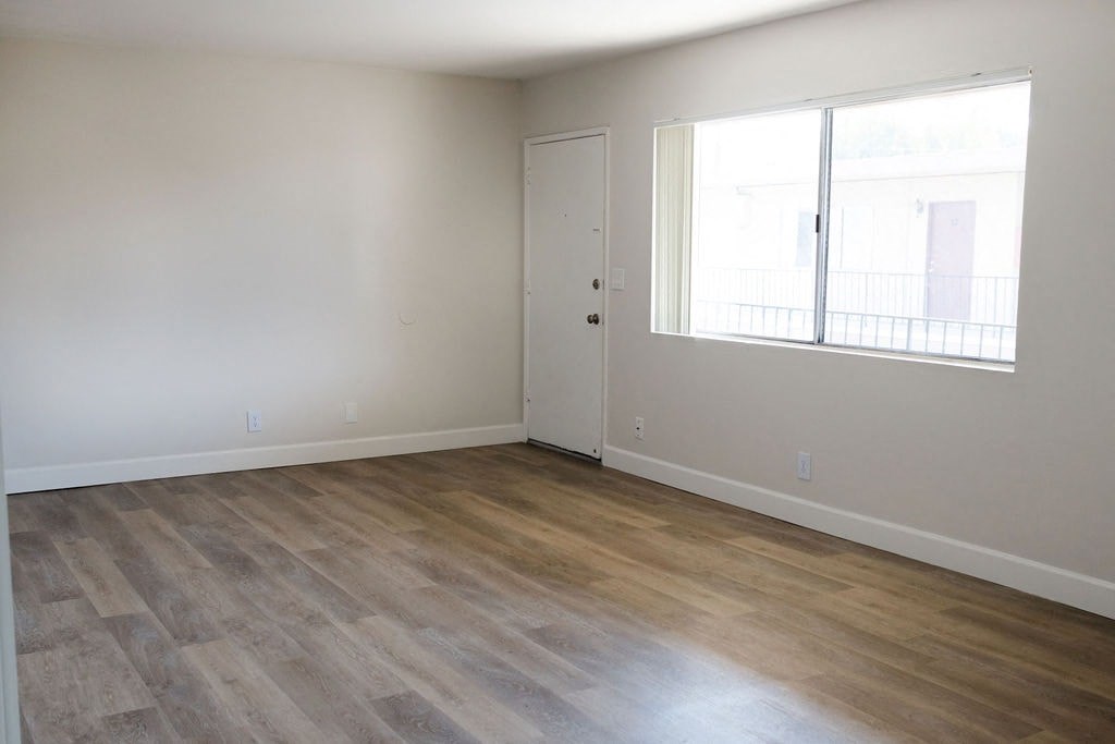 A room with a wooden floor and a window with a view of a building outside.