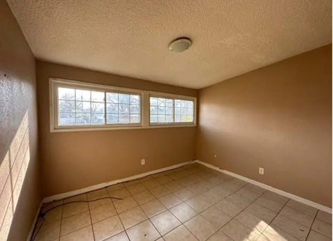 an empty living room with a large window and a tiled floor