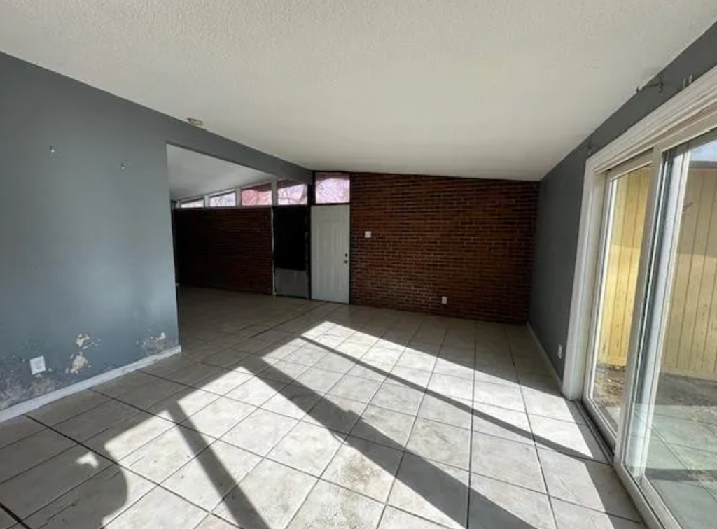 an empty living room with a tile floor and a brick wall