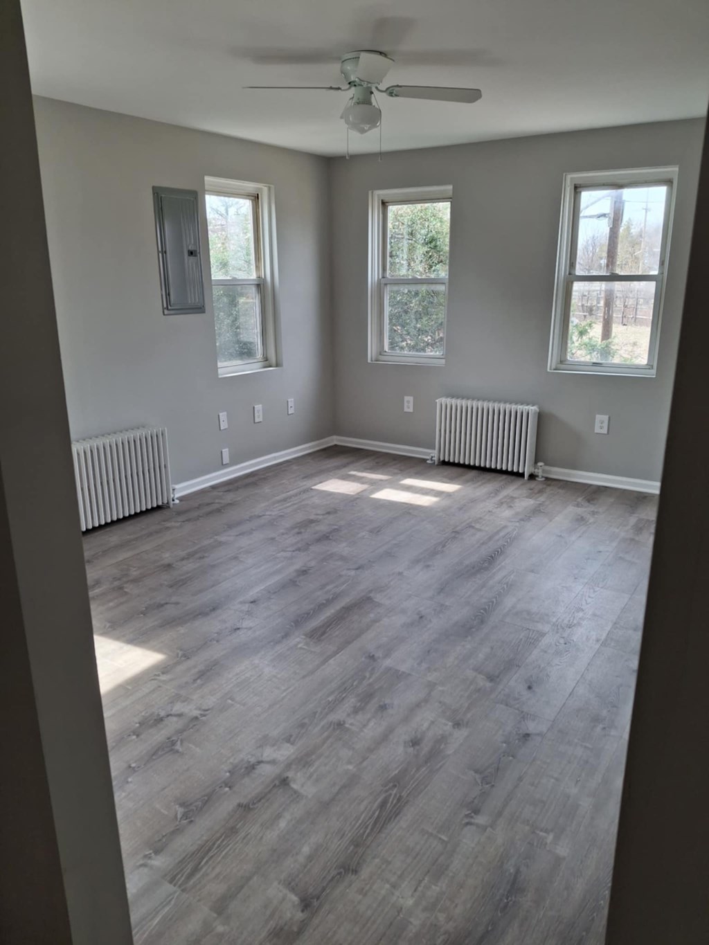 A room with a ceiling fan and three windows.