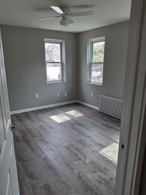 A room with a ceiling fan and two windows.
