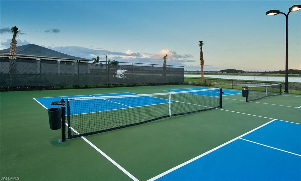 a tennis court with a fence and water in the background