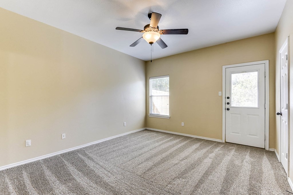 an empty living room with a ceiling fan and a door