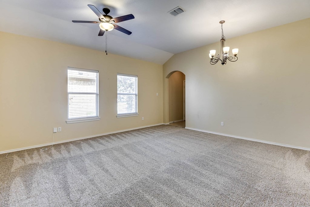 an empty living room with a ceiling fan and two windows