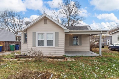 a small tan house with a porch and a yard