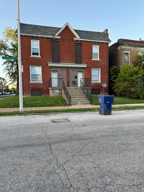 A red brick house with a blue trash can in front.