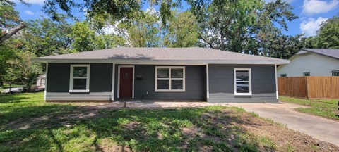 a small gray house with a yard and a driveway