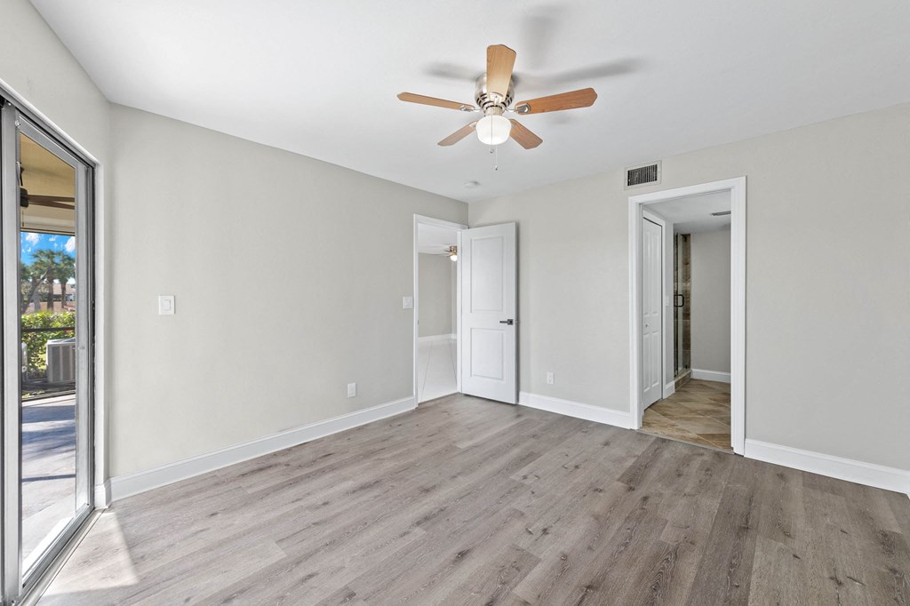 an empty living room with a ceiling fan and a door to a hallway