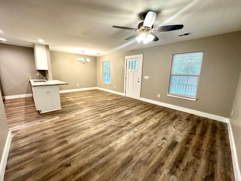 an empty living room with a ceiling fan and a kitchen