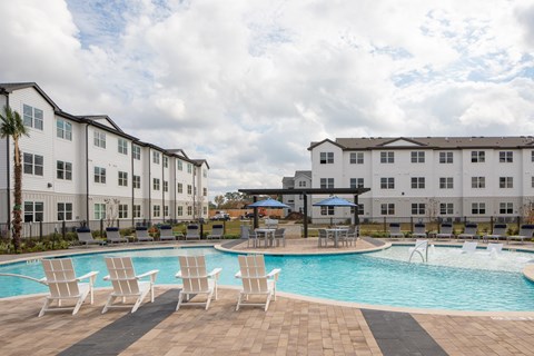 a swimming pool with chairs and umbrellas in front of apartment buildings