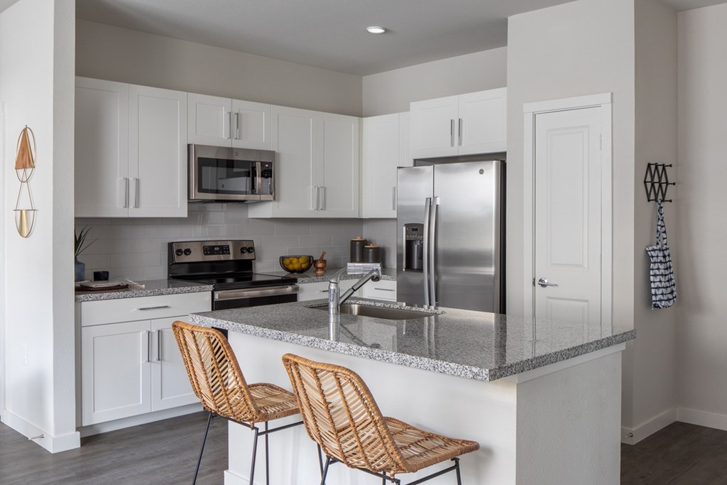 a kitchen with white cabinets and a counter with two chairs