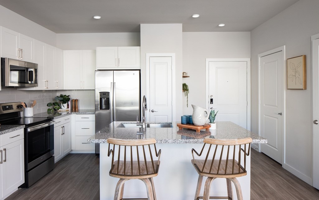 a kitchen with white cabinets and a island with two chairs