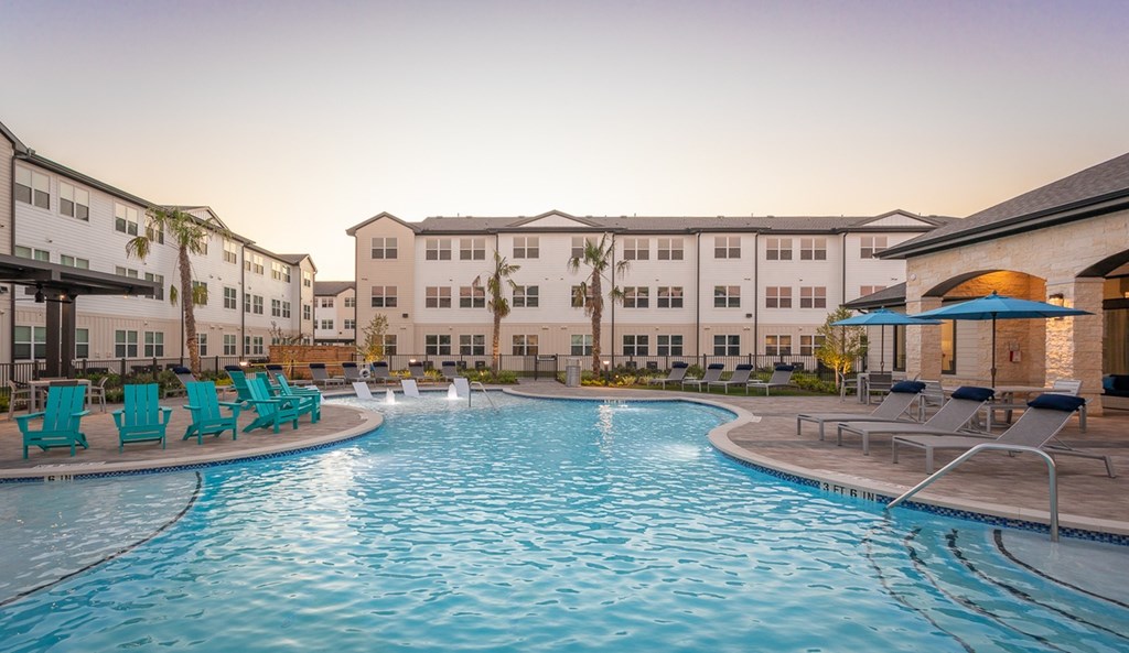a swimming pool with chairs and umbrellas in front of apartment buildings