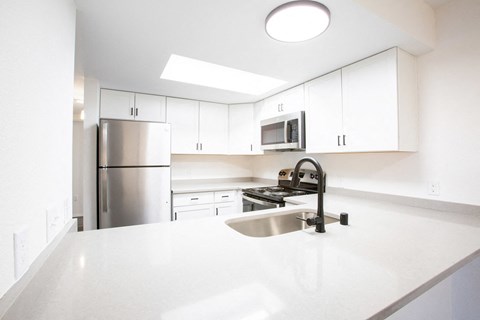 a white kitchen with stainless steel appliances and white counter tops
