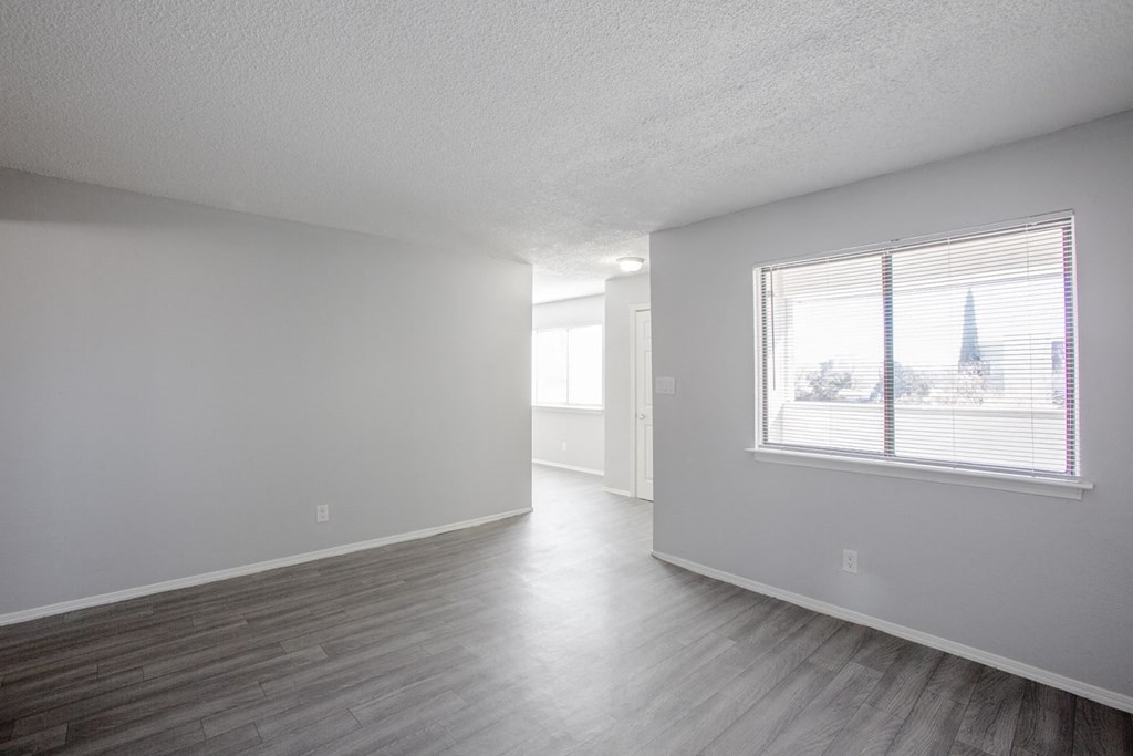 the living room and dining room of an apartment with white walls and a window