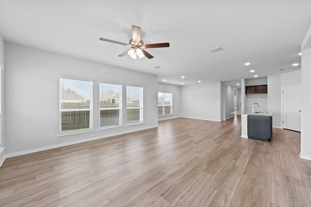 an empty living room with a ceiling fan and large windows