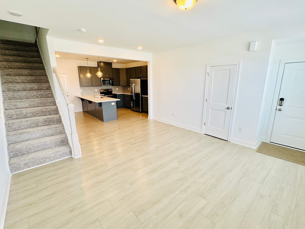 an empty living room with a staircase and a kitchen