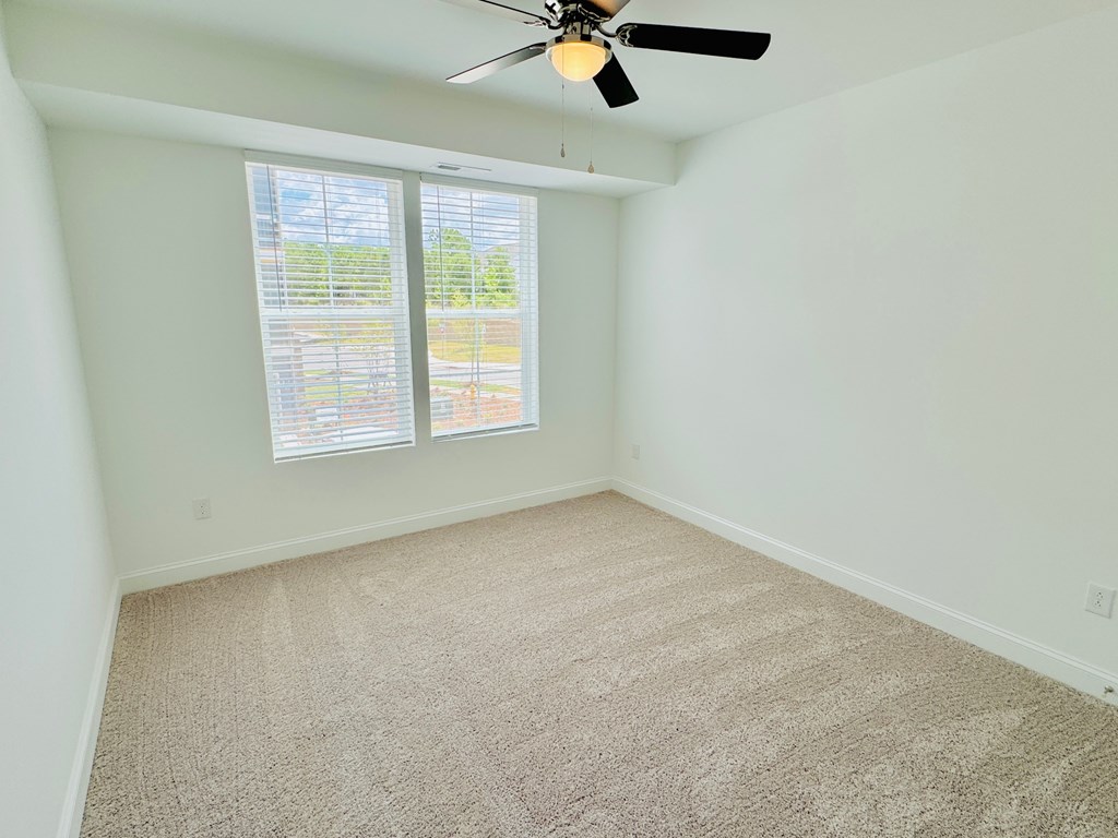 an empty room with two windows and a ceiling fan