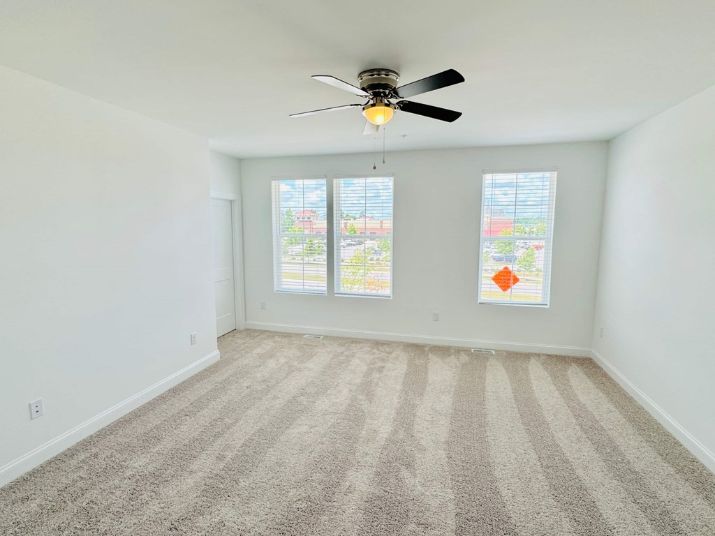 an empty living room with a ceiling fan and three windows