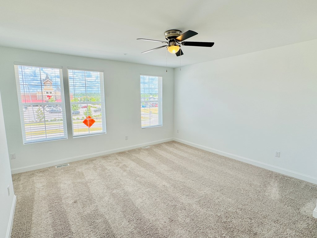 an empty living room with a ceiling fan and three windows