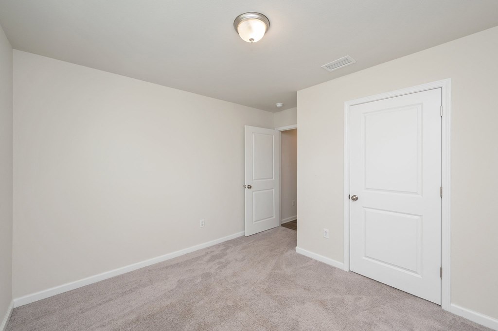 a bedroom with white walls and carpet and a door to a closet
